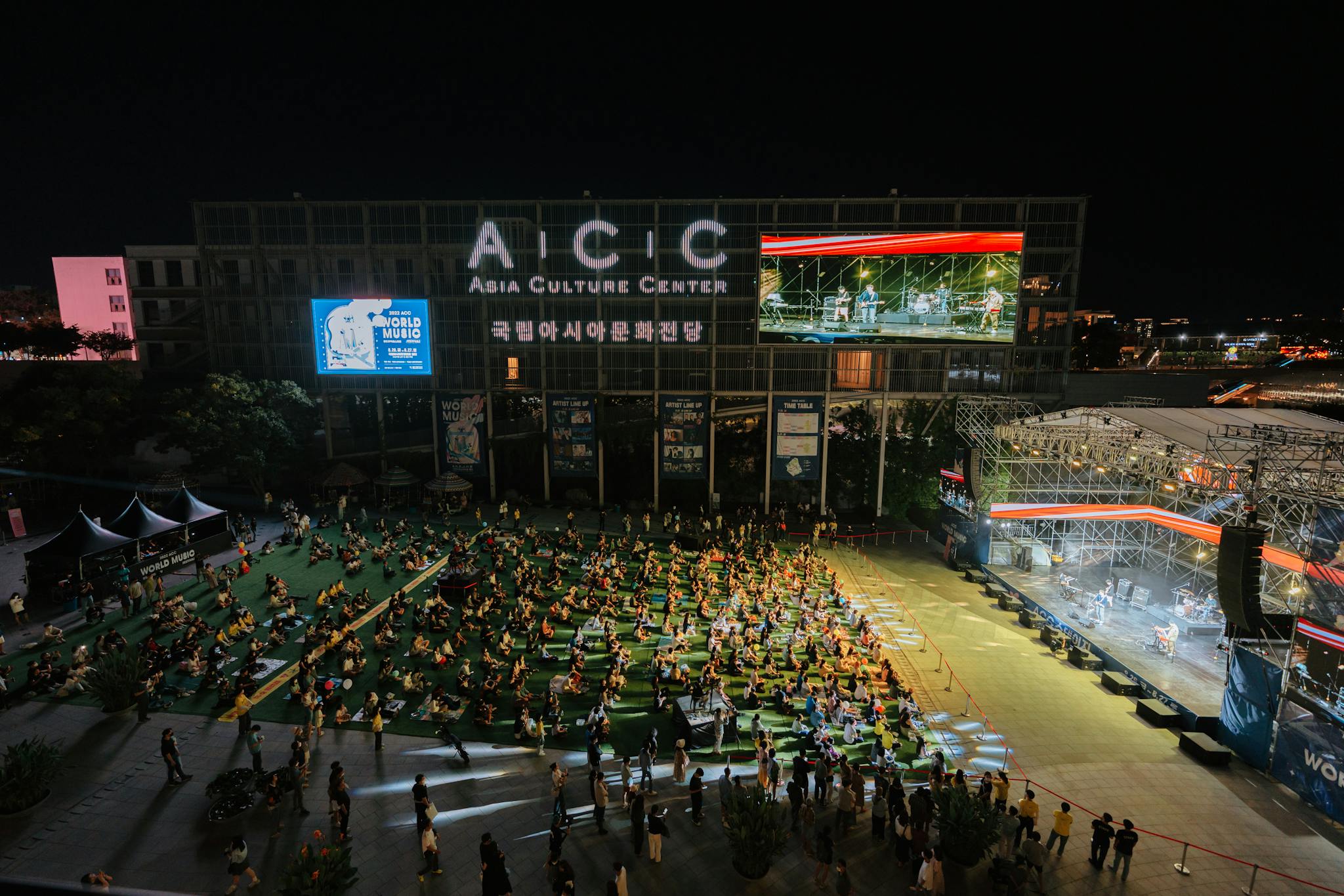 A vibrant outdoor concert at the Asia Culture Center, bustling with a lively crowd at night.
